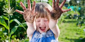 1 laughing child sticking her mud covered hands in front of her