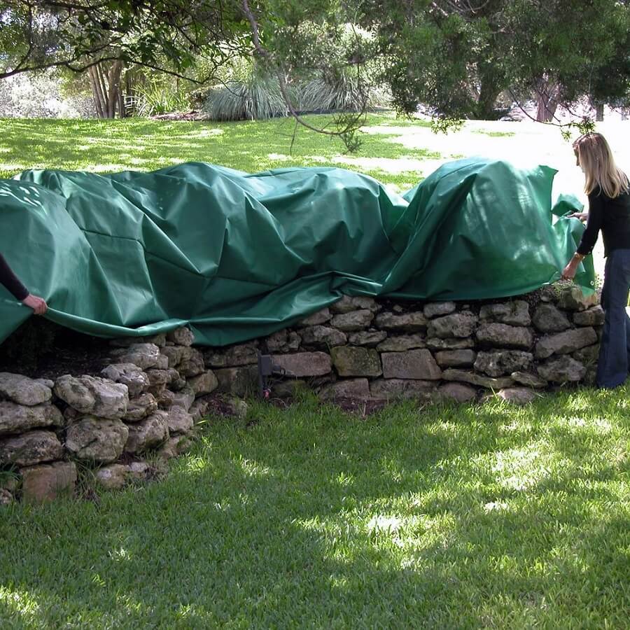 two people using a large blanket to cover some plants