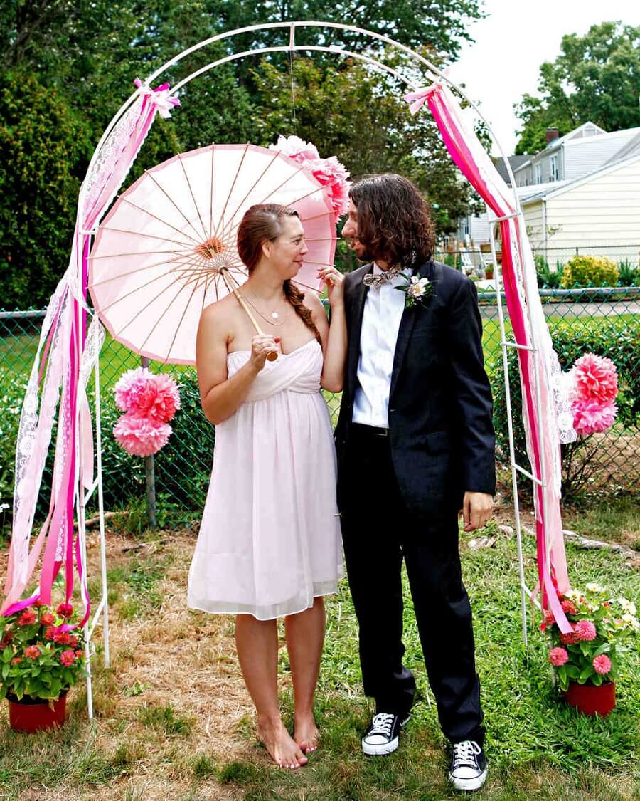 couple standing in front of a trellis decorated with ribbons and pom-poms